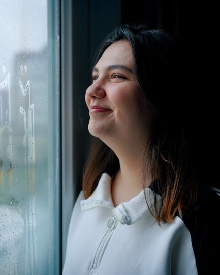 Portrait of a smiling woman after satisfactory adhd consultation at ICT Psychiatry looking out a rainy window, creating a serene and contemplative mood