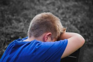 A sad child sitting alone, showing signs of persistent sadness with a downcast expression.