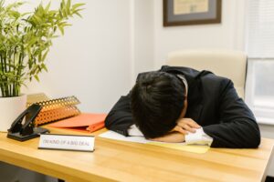 A person sitting at a desk with their head down, showing signs of low motivation and fatigue.