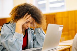 A person sitting in front of a laptop, appearing distracted and having difficulty concentrating while working.